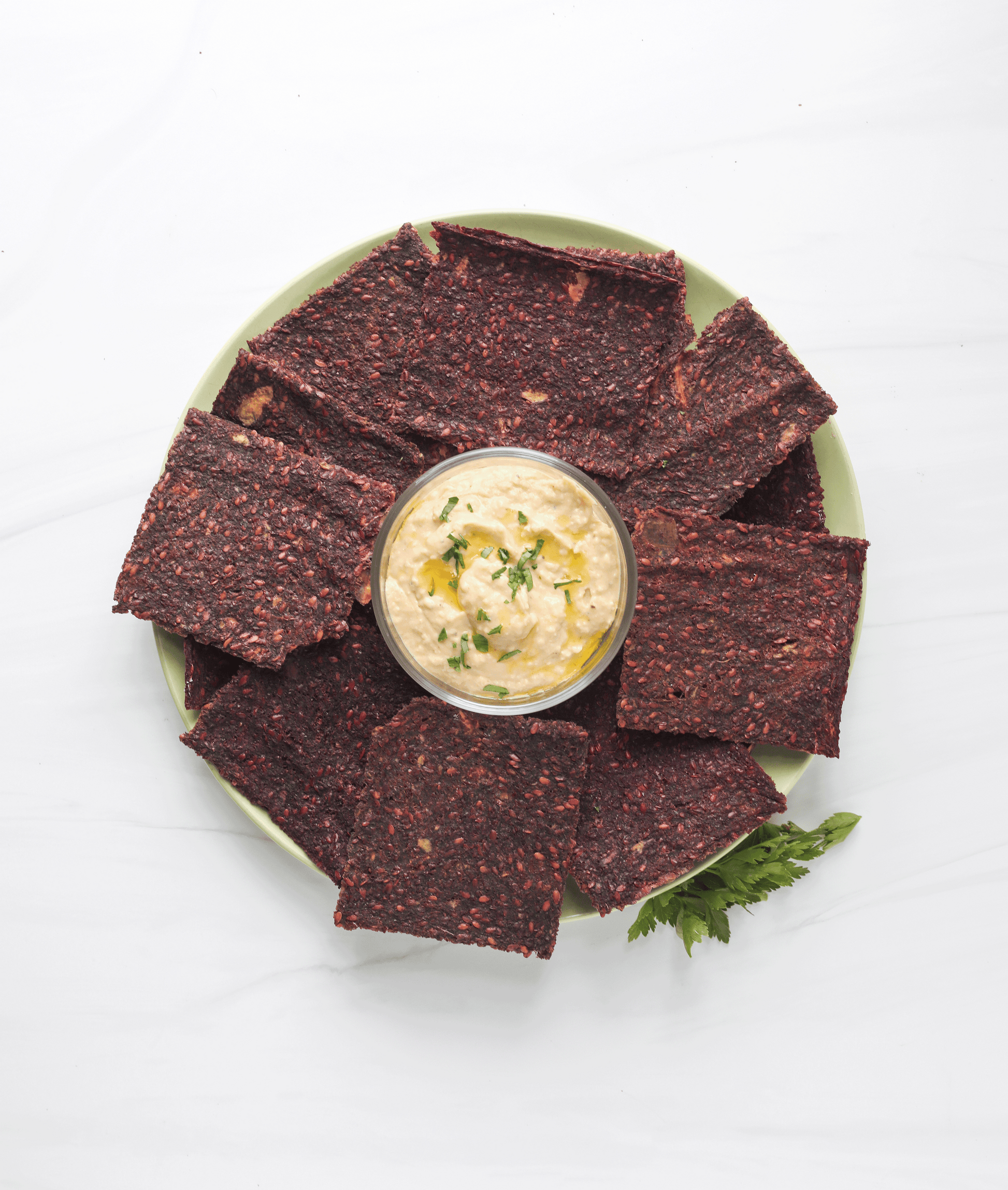 A plate of Kraut Krackers surrounding a bowl of hummus.